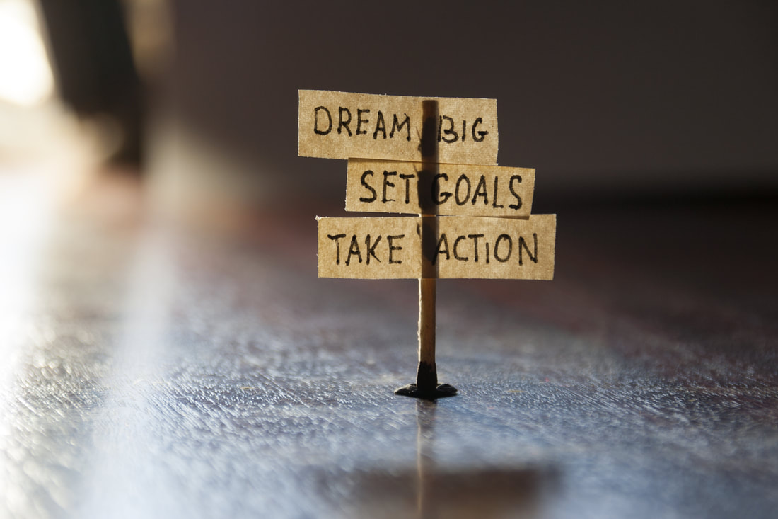 Small sign post that says Dream Big, Set Goals, Take Action